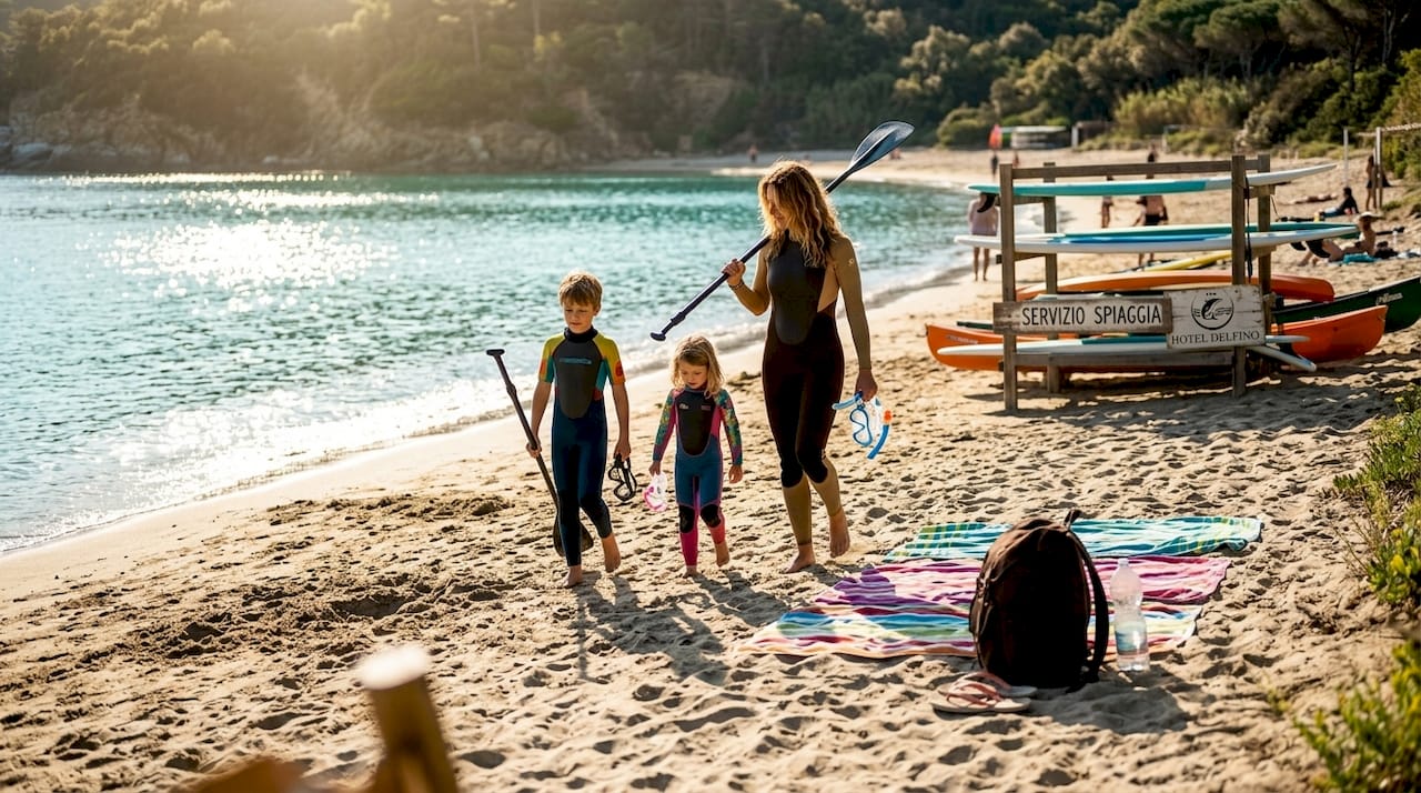 Una famiglia si gode una giornata al mare sull’Isola d’Elba, tra tavole da SUP e attrezzatura per snorkeling sulla spiaggia.